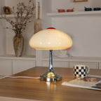 Warm light glows through the white scalloped shade of this Clérachic lamp, on a wooden desk with a checked mug and a magazine.