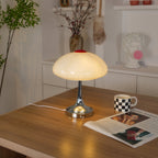 Lit Clérachic lamp on a wooden desk, a checked mug and open magazine beside it and a shelf of decor behind.