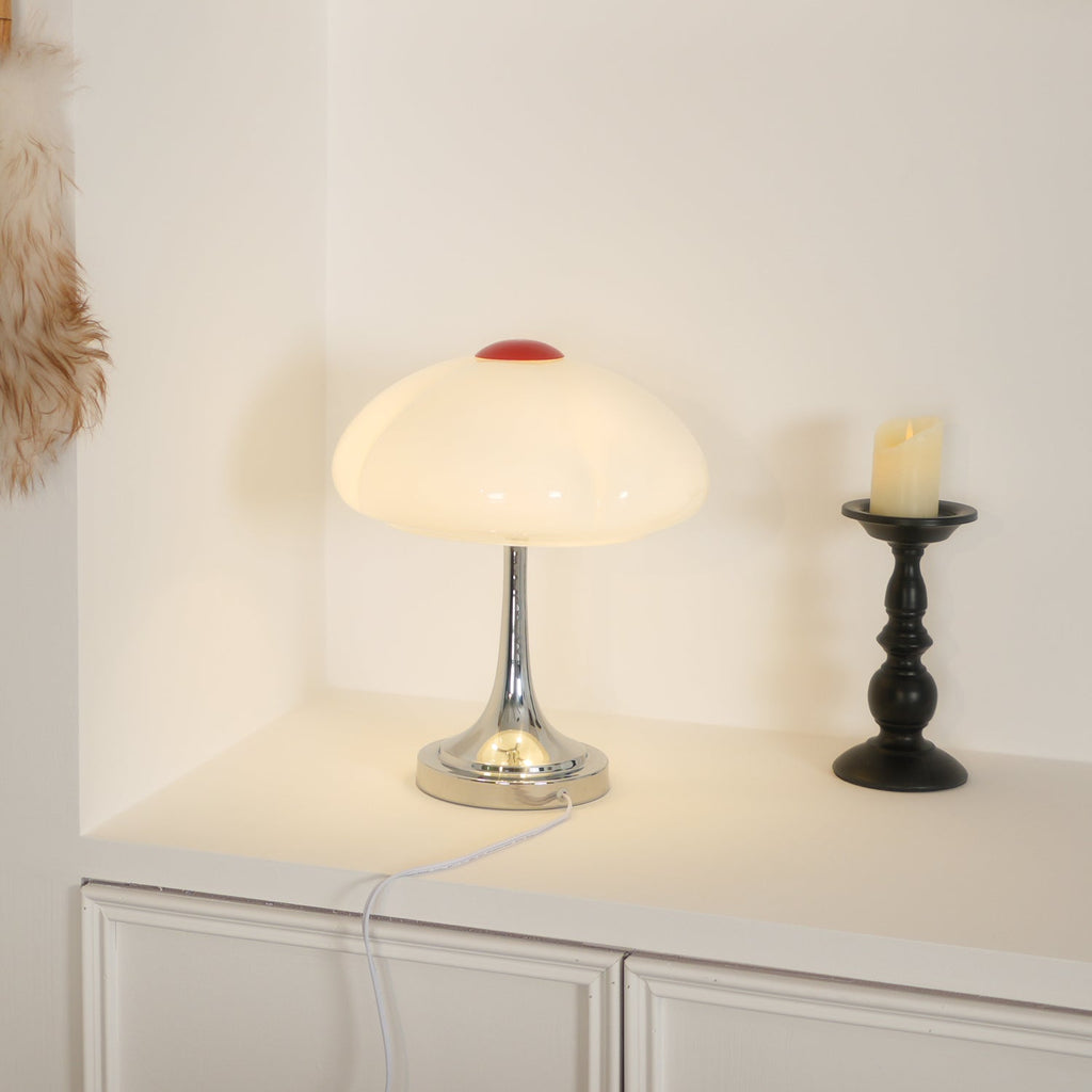 On a white sideboard, this Clérachic lamp glows softly beside a black candlestick, with its white cord trailing down.
