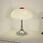 Soft-lit Clérachic table lamp against a pale wall, the chrome base reflecting the warm glow of the scalloped glass shade.