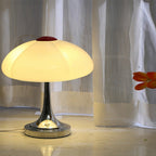 Lit Clérachic table lamp in front of sheer white curtains, with an orange flower at the right edge of the frame.