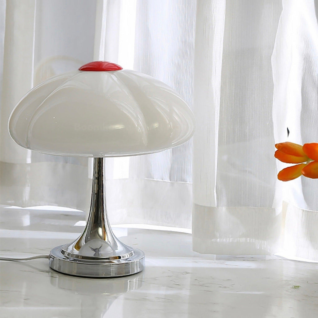 Unlit Clérachic table lamp in front of sheer white curtains, its white glass shade and red cap above the chrome stem.