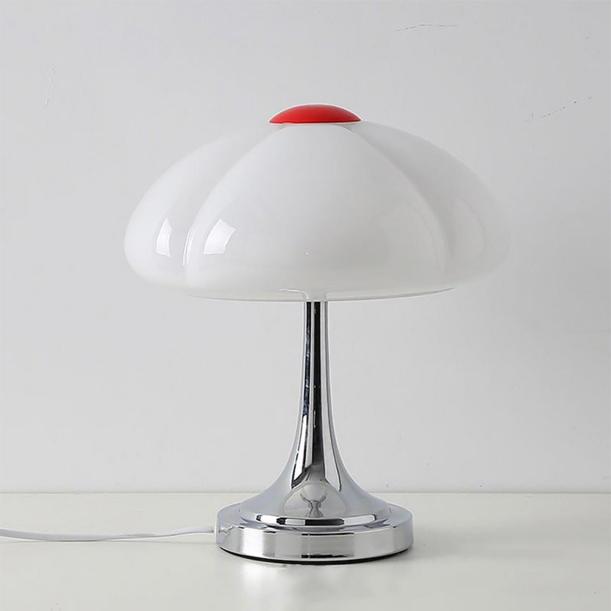 Unlit white scalloped shade with a red cap on this Clérachic lamp, standing on a pale surface against a grey wall.