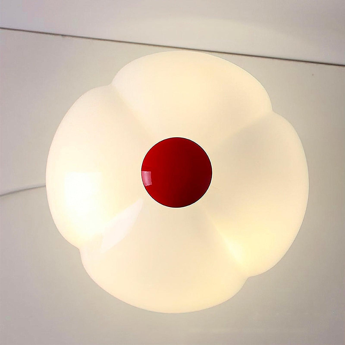 Top-down view of the lit, petal-lobed shade of this Clérachic lamp, with the red cap at the centre.