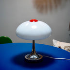This Clérachic table lamp, unlit, on a bright blue table with a white cord and a cushion in the background.