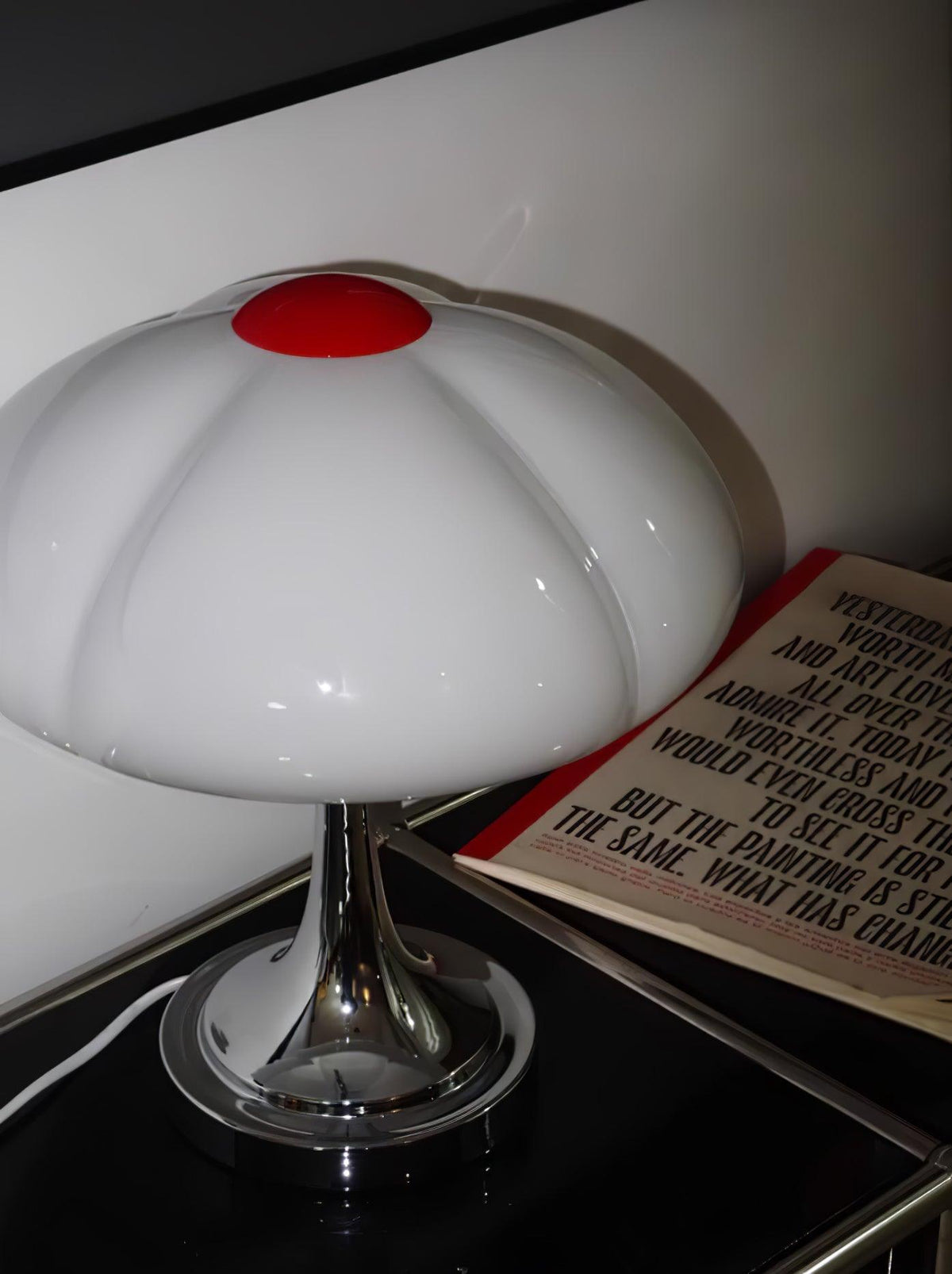 Clérachic table lamp, unlit, on a black side table, with a book beside it and the red cap in the centre of the shade.