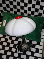 This Clérachic lamp on a black-and-white checked floor, in front of a green fluffy cushion, its glass shade unlit.