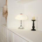 This Clérachic table lamp lit on a white worktop, a black candlestick with a candle standing to its right.