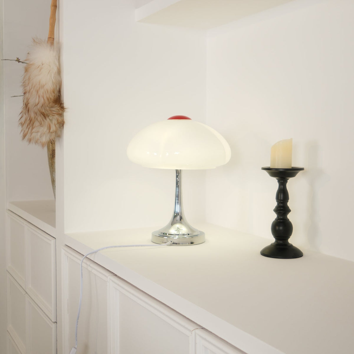 This Clérachic table lamp lit on a white worktop, a black candlestick with a candle standing to its right.