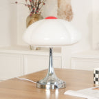 Close view of the white scalloped shade on this Clérachic lamp, unlit, above a chrome stem on a wooden desk.