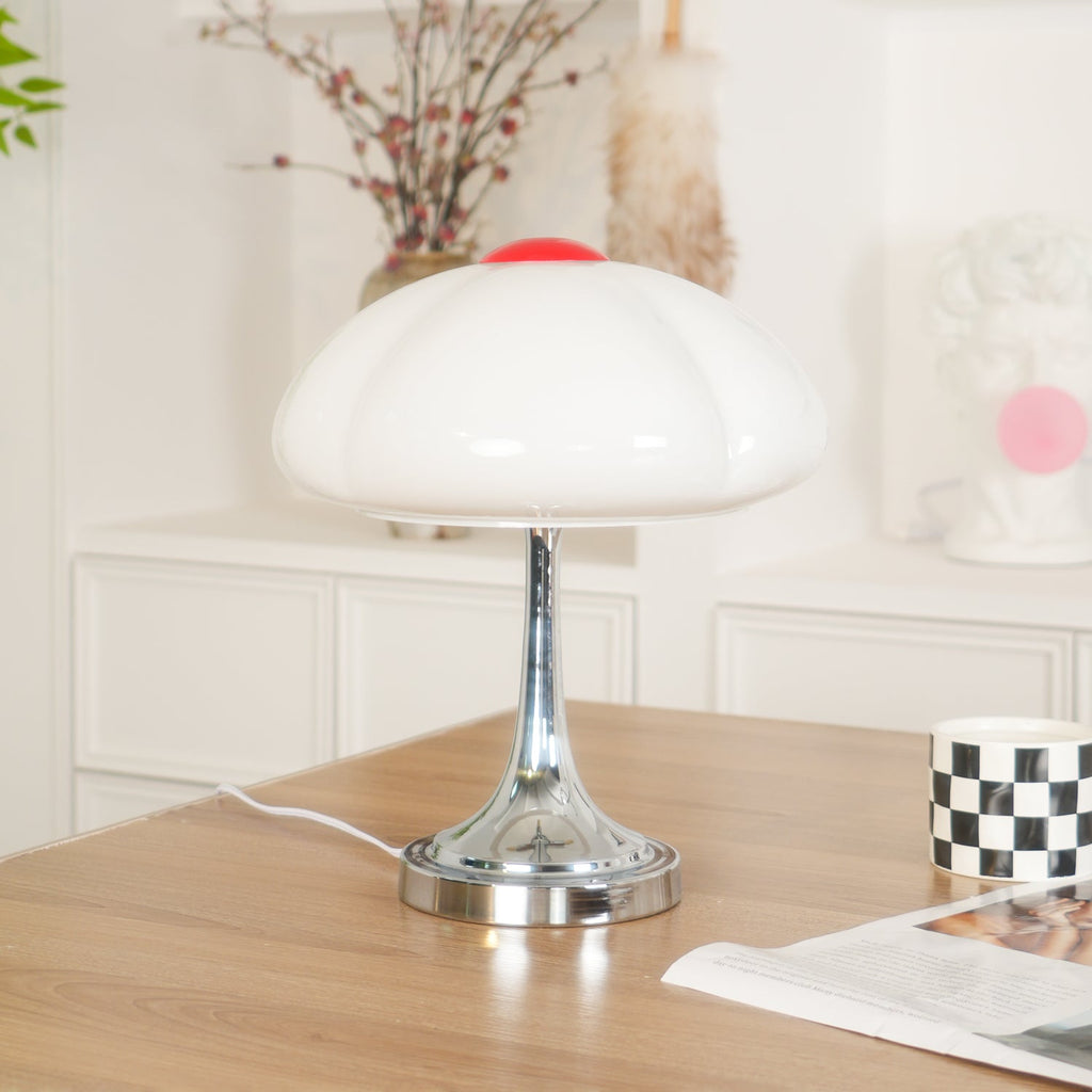 Clérachic lamp with a white glass shade on a wood desk, a checked mug and a magazine at the right, and a dried-flower vase behind.