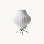 A white ribbed pear-shaped shade on a slim tripod stand, this Clérachic table lamp shown unlit on a plain off-white backdrop.