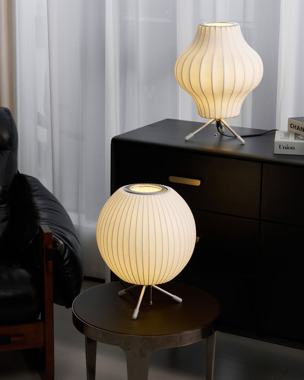 The same pair of Clérachic table lamps lit, a warm pear shape on the cabinet and a round shade on the side table below.