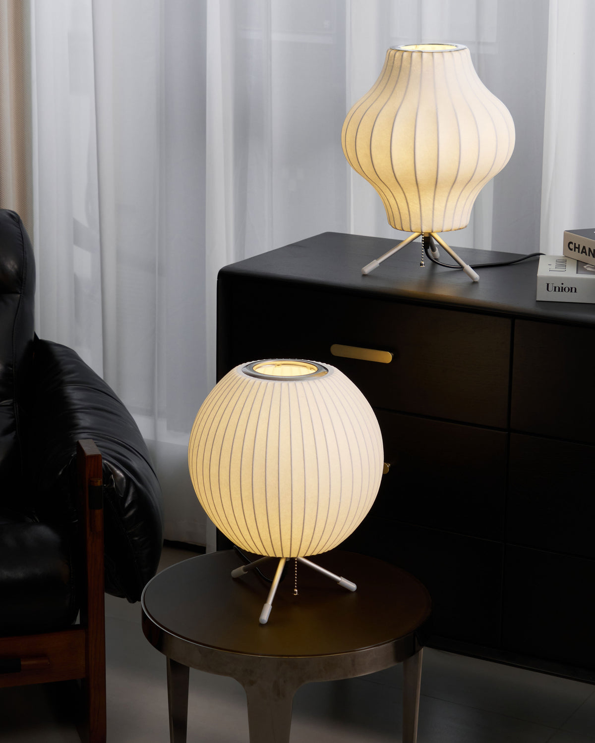 The same pair of Clérachic table lamps lit, a warm pear shape on the cabinet and a round shade on the side table below.