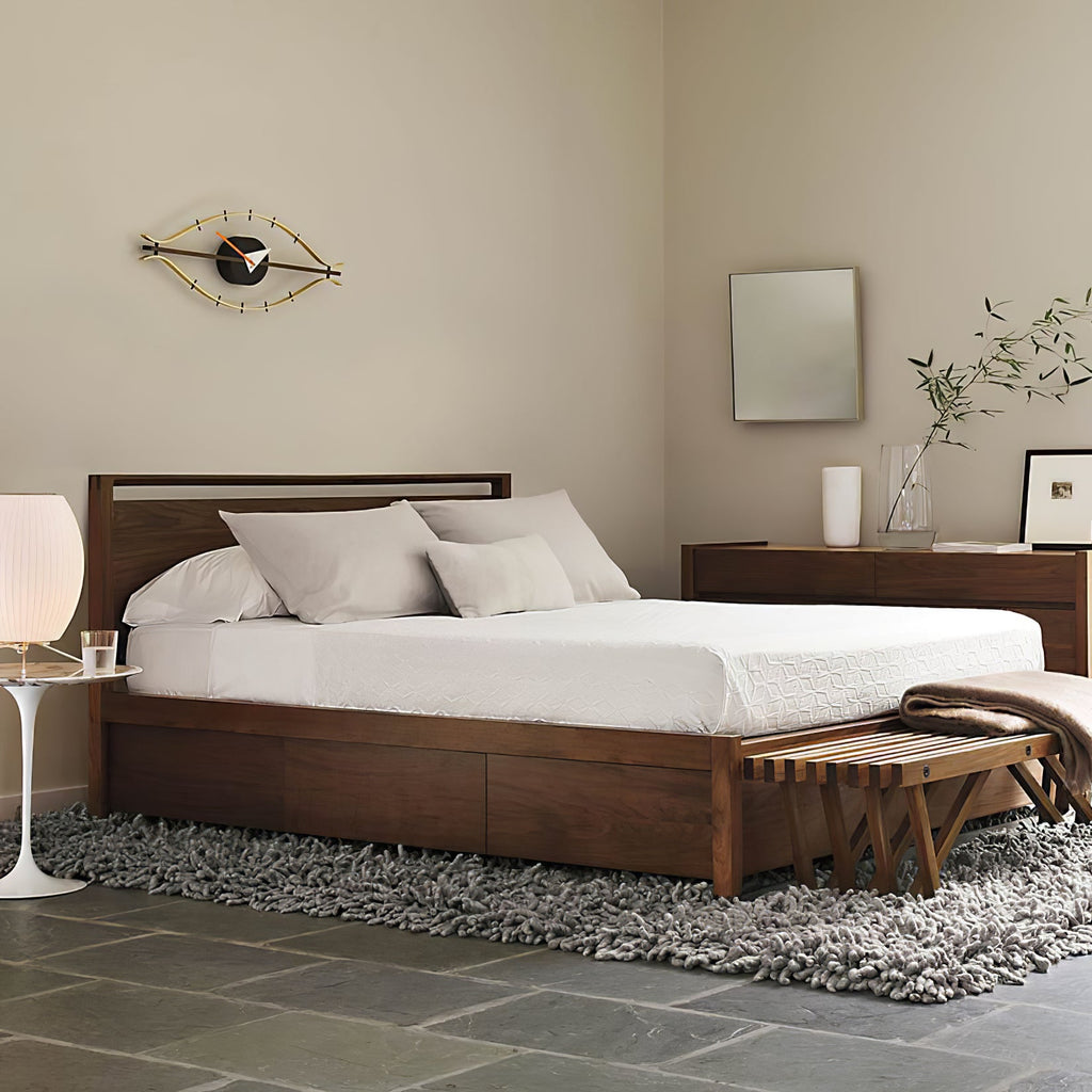A white lamp glows on a small white side table beside a wooden bed in a calm bedroom, in this Clérachic room scene.
