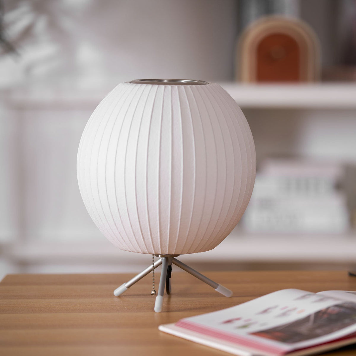 Close view of an unlit round white shade on three slim legs, this Clérachic table lamp resting on a light wooden desk.