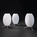 Three unlit oval white Clérachic table lamps of different sizes stand on a dark floor against a black backdrop.