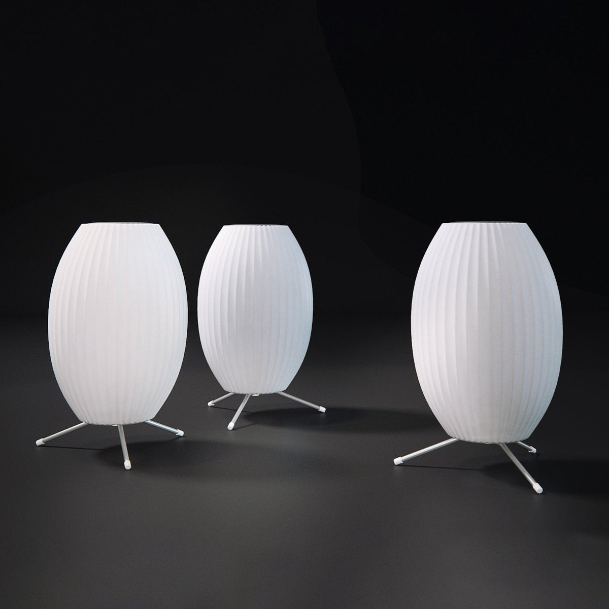 Three unlit oval white Clérachic table lamps of different sizes stand on a dark floor against a black backdrop.