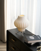 A pear-shaped Clérachic table lamp, lit, on a black chest with brass handles, beside an art book and a few white flowers.