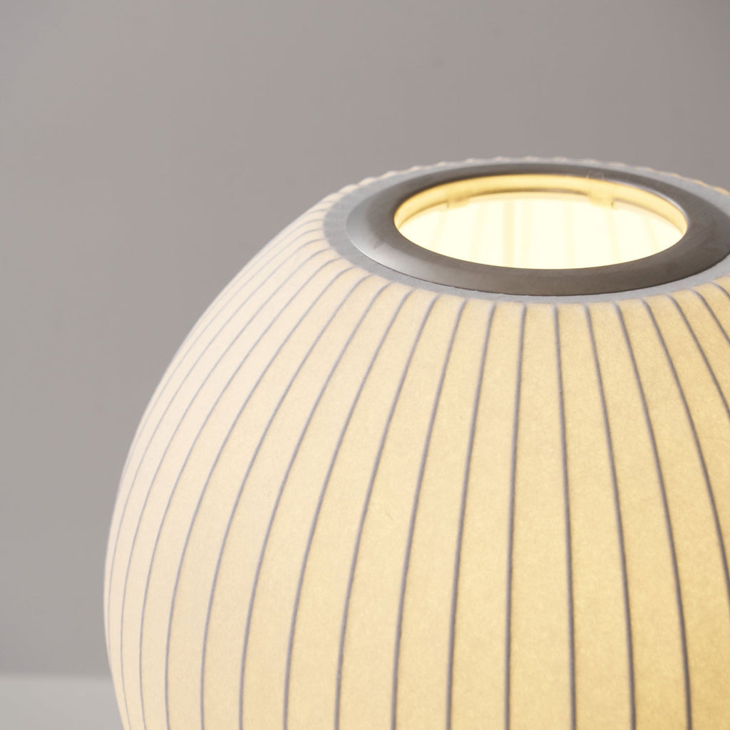 Close view of the round, ribbed shade of this Clérachic table lamp, glowing, with its metal ring around the top opening.
