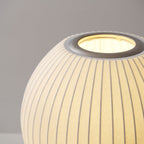 Close view of the round, ribbed shade of this Clérachic table lamp, glowing, with its metal ring around the top opening.