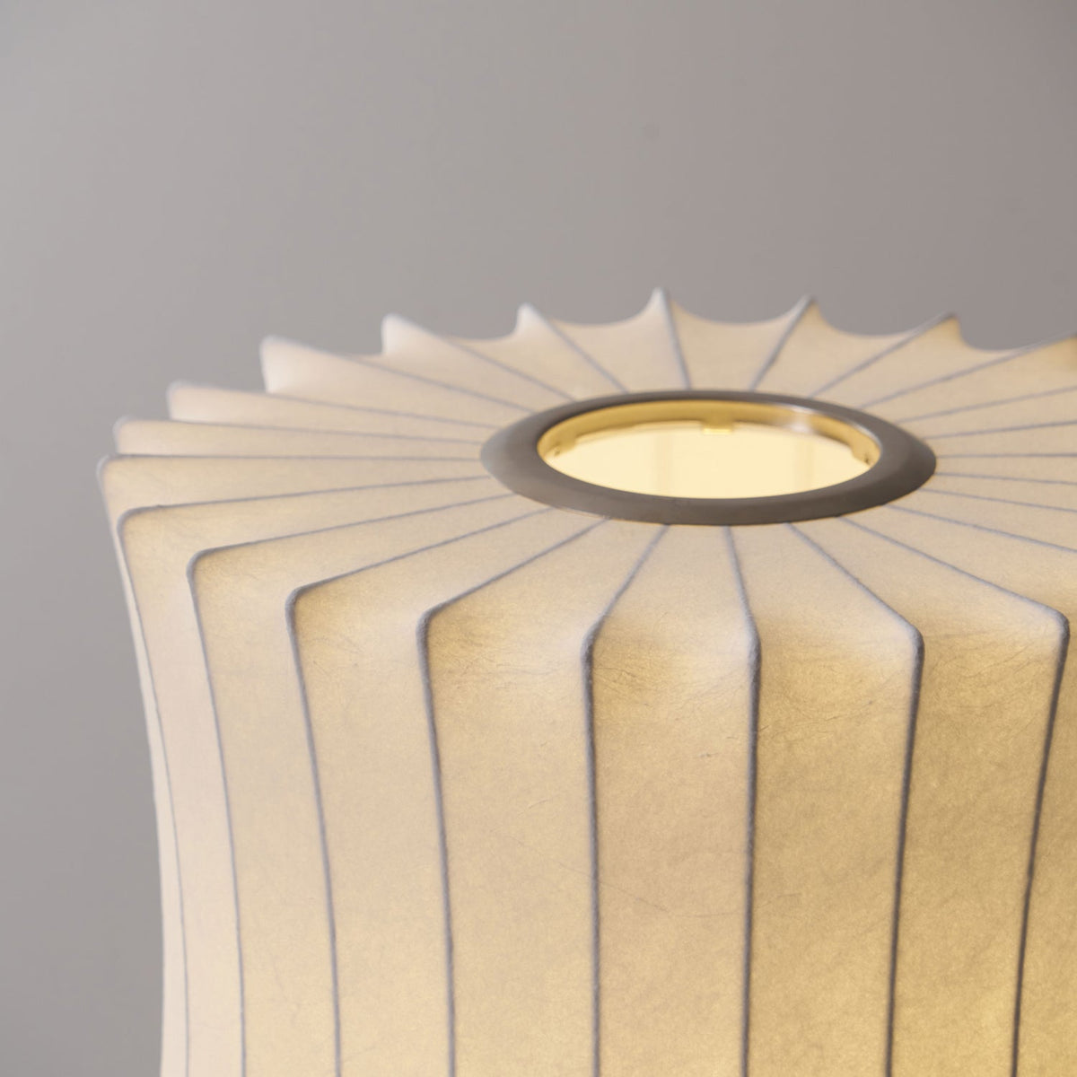 Close view of the pleated top edge and metal ring of a waisted shade on this Clérachic table lamp, softly lit from inside.