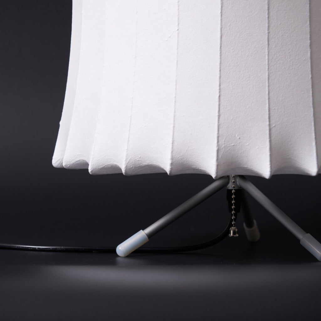 Close view of the lower edge of the white ribbed shade and the tripod legs with white tips on this Clérachic table lamp.