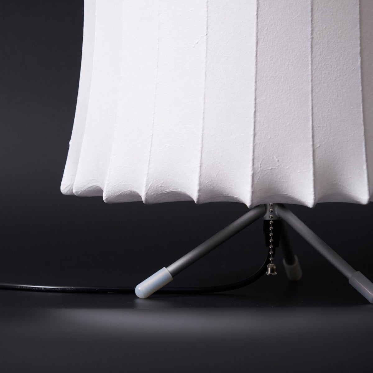 Close view of the lower edge of the white ribbed shade and the tripod legs with white tips on this Clérachic table lamp.