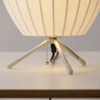 The slim tripod legs, white tips, pull chain and black cord beneath the round shade of this Clérachic table lamp.