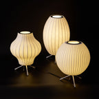 Three Clérachic table lamps, a pear, an oval and a round shade, glow together against a black backdrop on a dark floor.