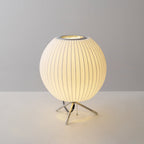 Round Clérachic table lamp lit on a grey set, warm light spilling under its shade and onto the white surface below.