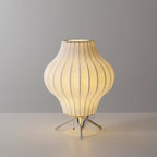 A pear-shaped Clérachic table lamp, lit, glowing warm on a pale grey set with light pooling around its tripod legs.