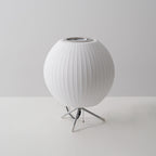 An unlit round Clérachic table lamp on a grey set, its ribbed white shade sitting just above three slim legs.