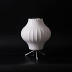 A pear-shaped white Clérachic table lamp, unlit, on a black set with a pull chain and a black cord at its base.