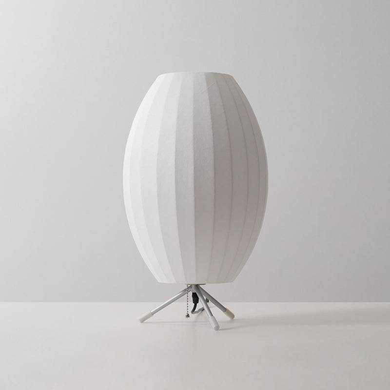 A tall oval white Clérachic table lamp, unlit, on a pale grey set, filling the frame with its ribbed shade.
