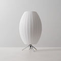 A tall oval white Clérachic table lamp, unlit, on a pale grey set, filling the frame with its ribbed shade.