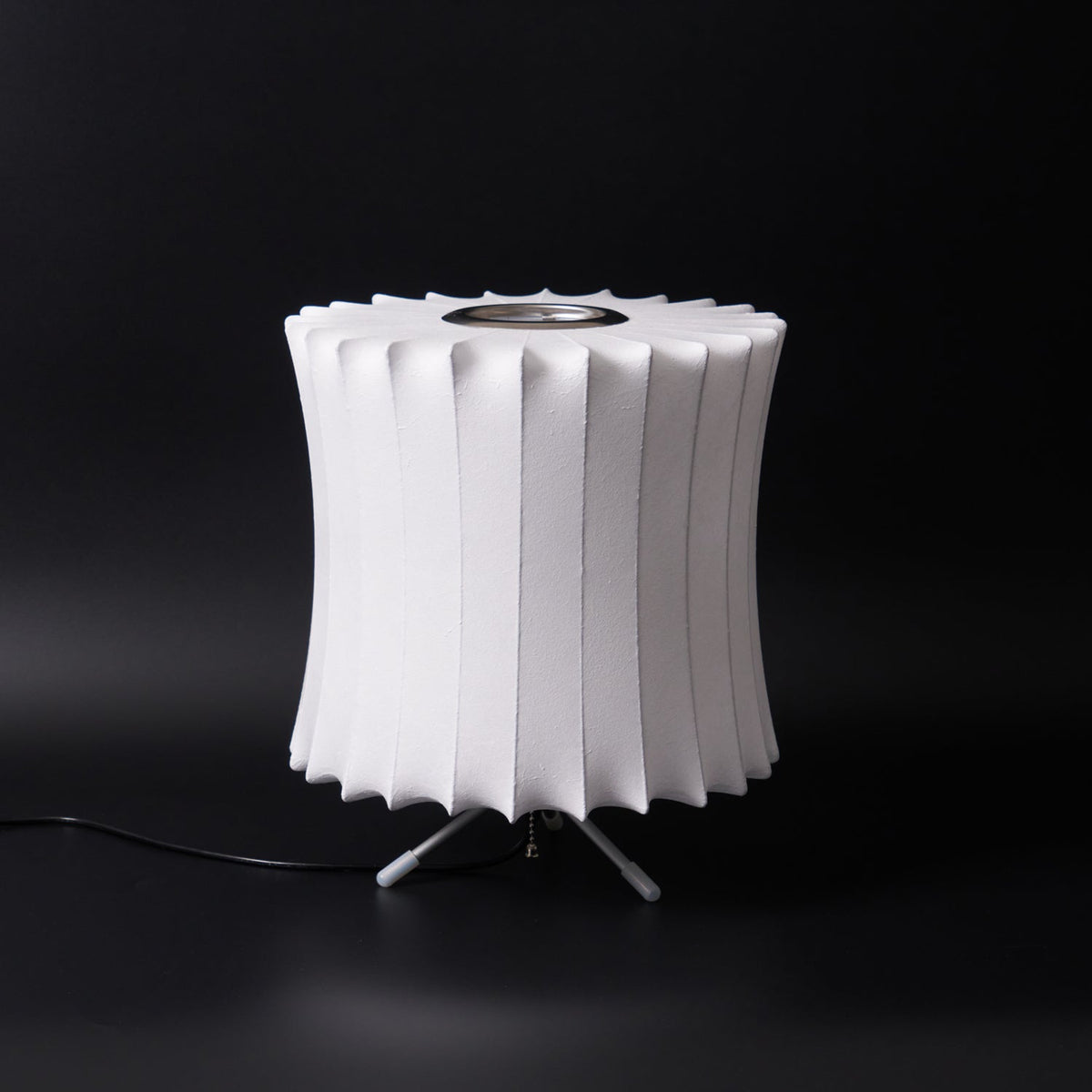 Unlit waisted white Clérachic table lamp on a black background, its pleated rim and ribbed shade clear to see.