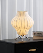 Pear-shaped Clérachic table lamp lit on a black drawer unit, a brass pull below and a stack of art books at the right.