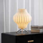 Lit pear-shaped Clérachic table lamp glowing warm on a black chest of drawers, with sheer curtains behind and art books beside it.