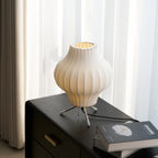 A white pear-shaped shade sits on a dark wooden chest by a curtained window, this Clérachic table lamp lit from within.