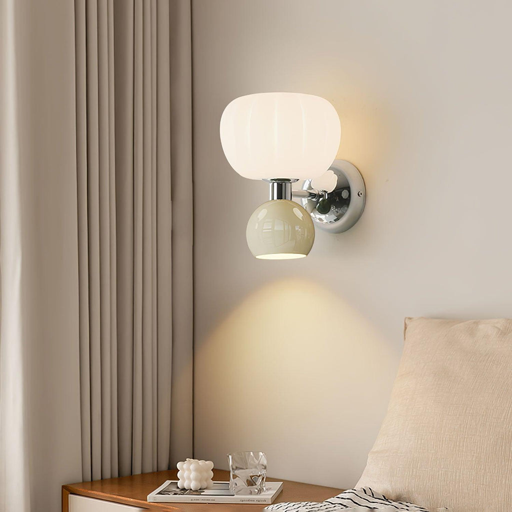 A Clérachic chrome wall light with a ribbed glass shade and a pale sage-grey ball lights a bedside corner beside long taupe curtains.