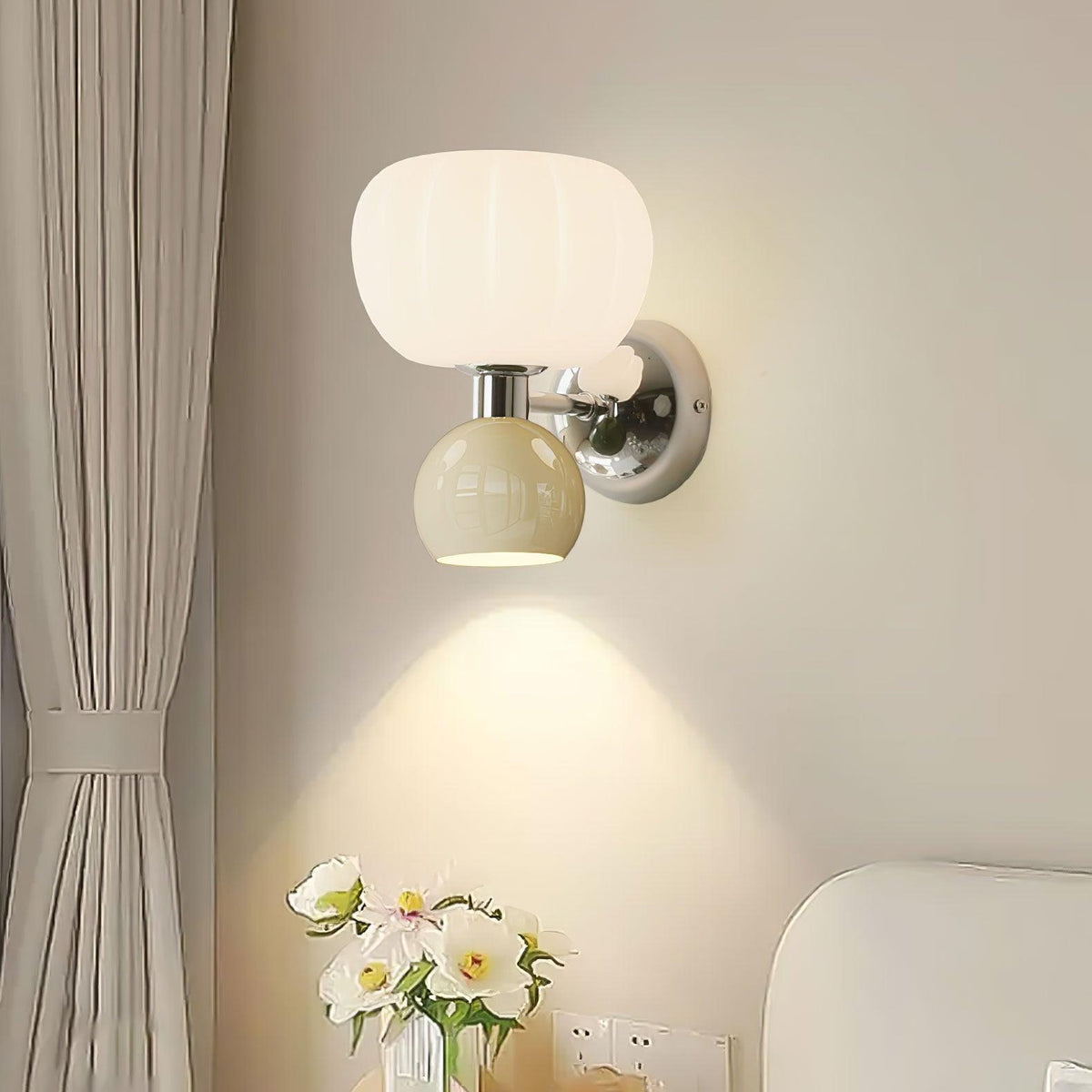 Close view of this Clérachic chrome wall sconce with a pale sage-grey ball, its downward beam falling on the wall above a vase of white flowers.