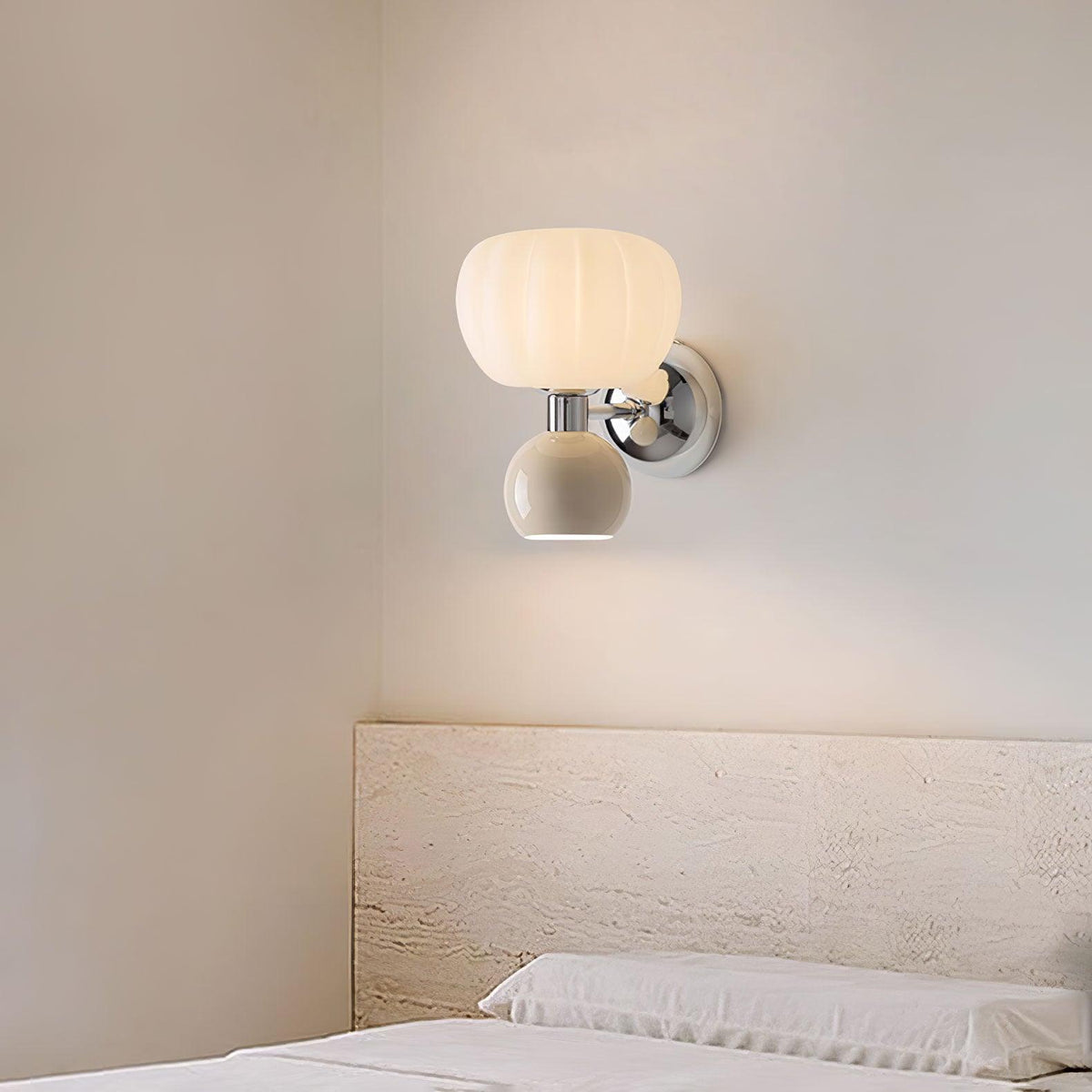 Above a low pale headboard, this Clérachic chrome wall light with a cream ball casts a soft glow down onto a grey-beige wall.