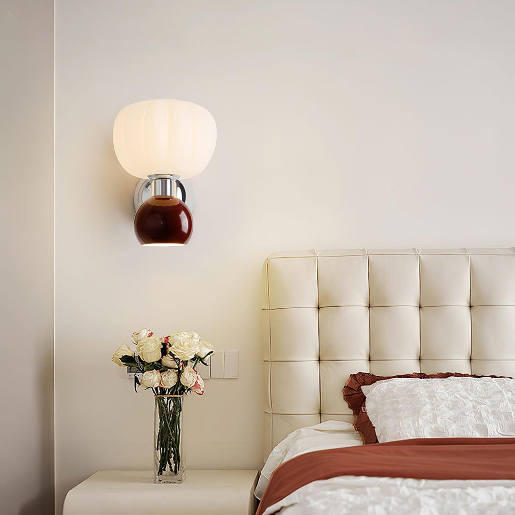 This Clérachic chrome wall light with a deep red ball hangs above a tufted cream headboard, with a vase of pale roses on the bedside.