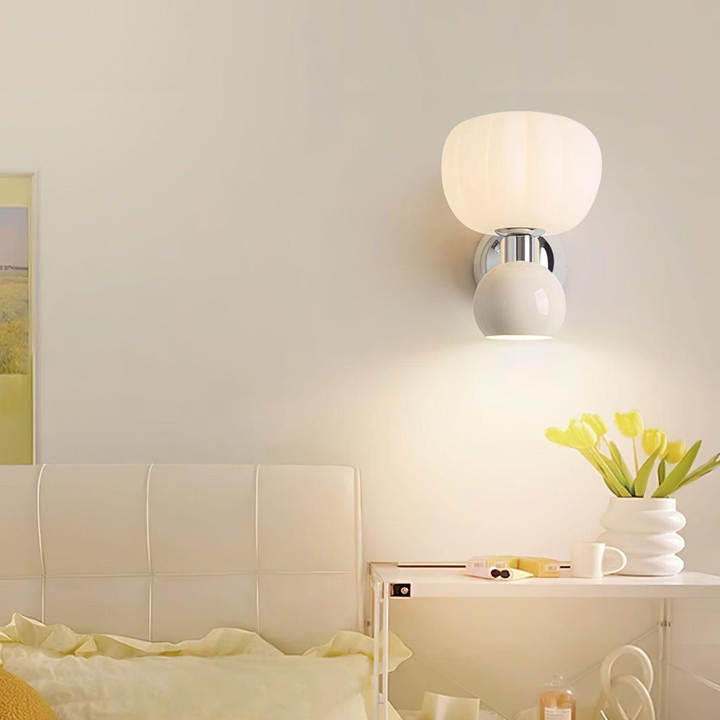 A Clérachic chrome wall light with a cream ball hangs above a bedside shelf with yellow tulips, beside a cream tufted headboard.