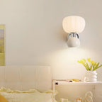 A Clérachic chrome wall light with a cream ball hangs above a bedside shelf with yellow tulips, beside a cream tufted headboard.