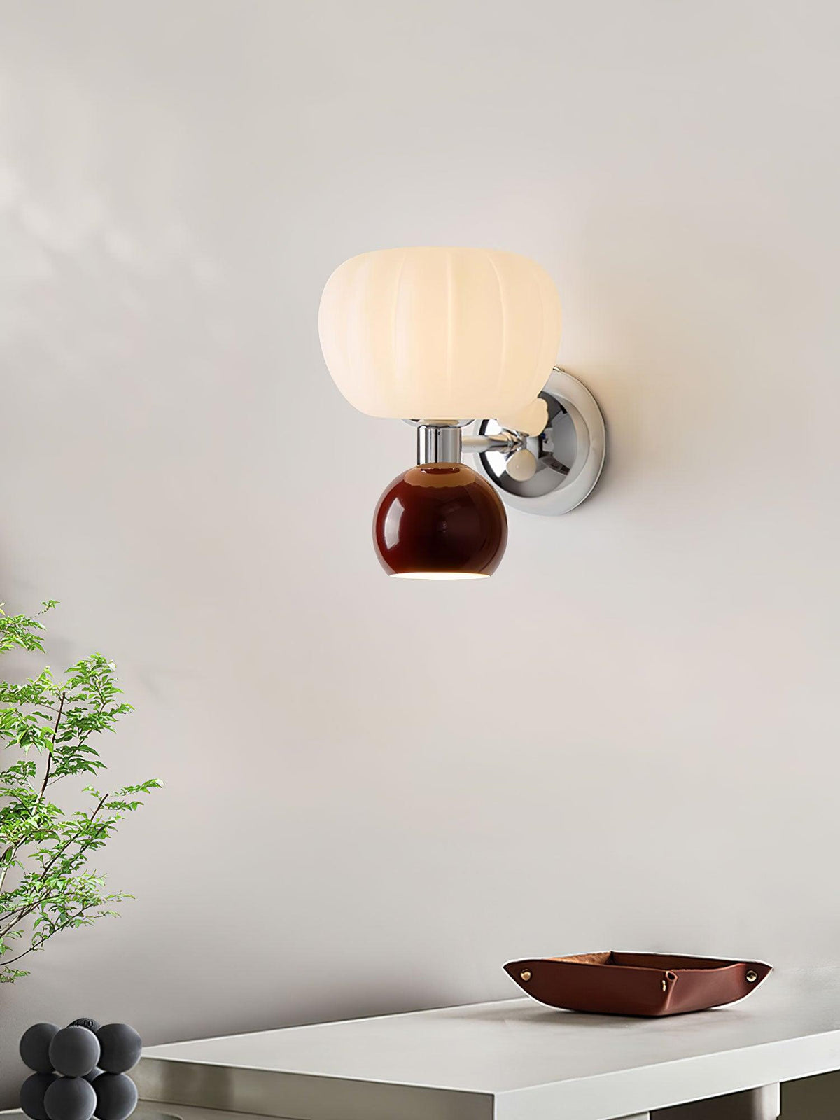 Seen from the side, this Clérachic chrome wall light with a deep red ball sits beside a small tree branch and a tray on a white desk.