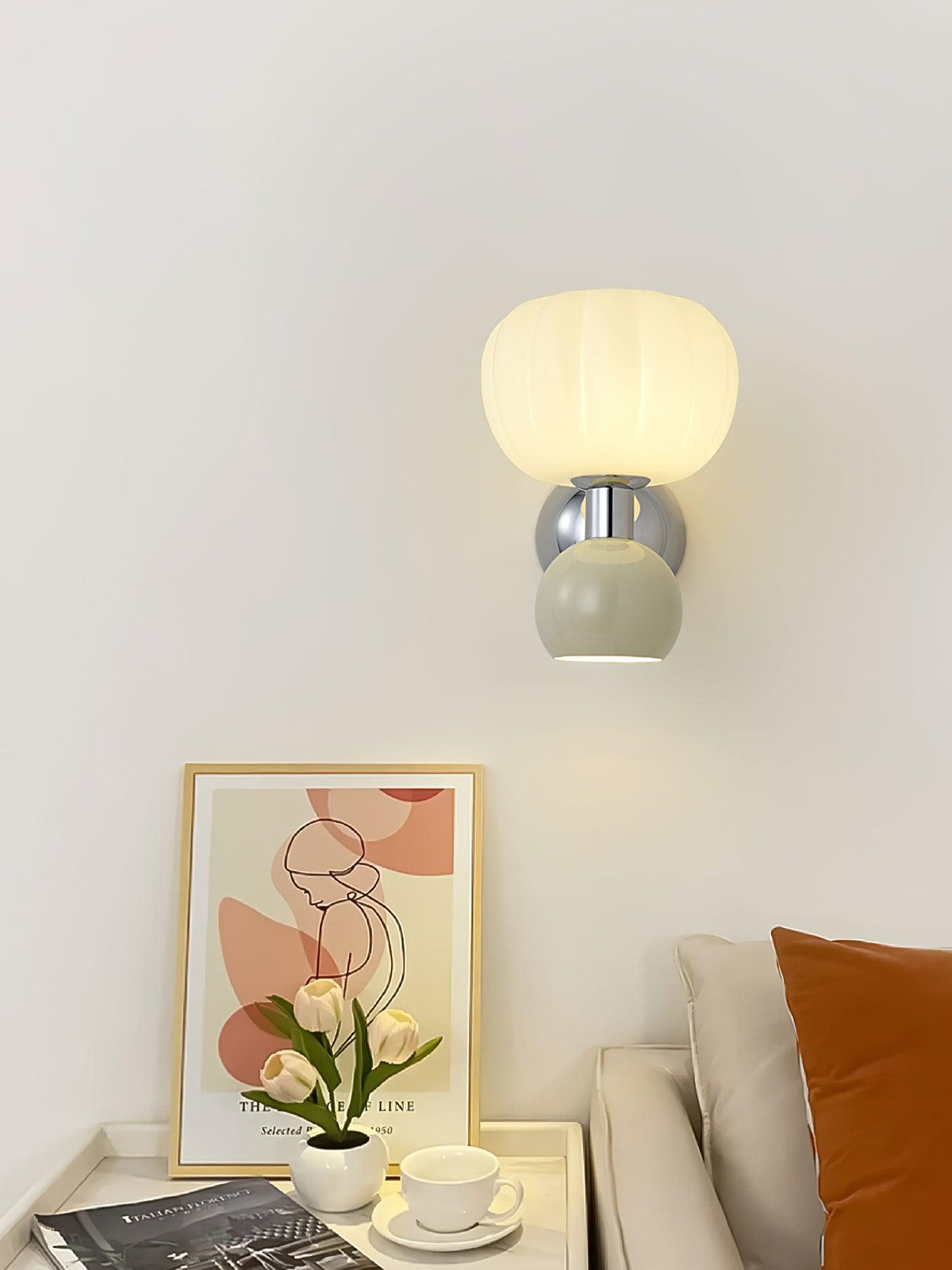 Above a side table with a framed abstract print and white tulips, this Clérachic chrome wall light with a pale sage-grey ball is lit.