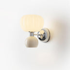 Close view of this Clérachic chrome wall light with a cream ball and ribbed glass shade, glowing against a pale backdrop.