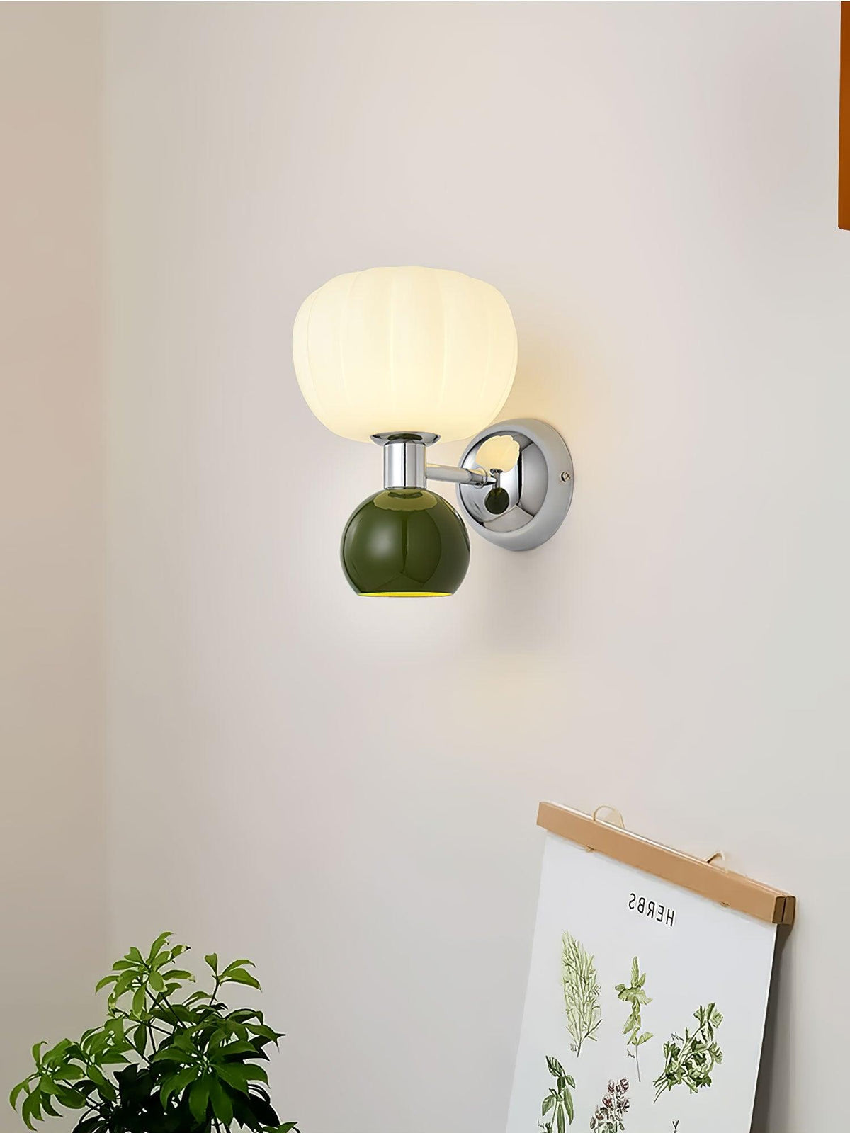 A dark-green ball under a ribbed glass shade on this Clérachic chrome wall light, beside a framed botanical print and a leafy plant.
